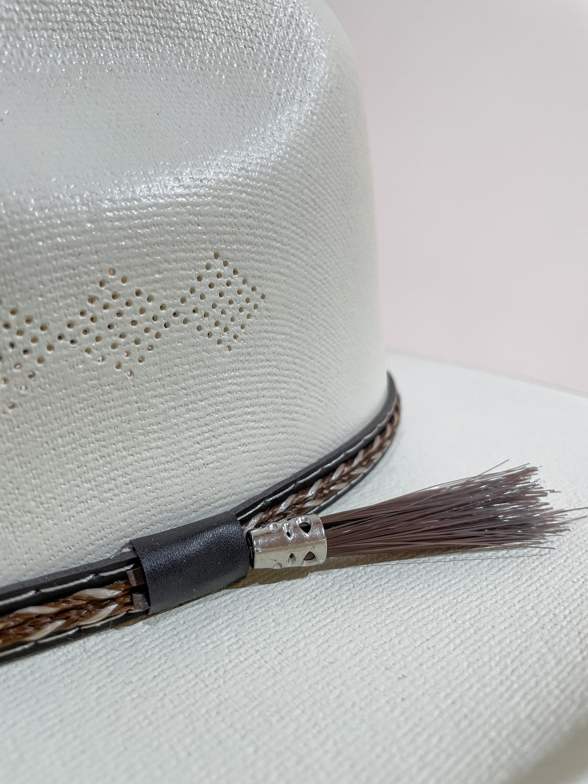 Closeup of a straw hat's crown and leather hatband with woven and tassel details