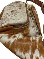 Close-up of light brown cow hair fanny pack showing front zippered pocket with natural cowhide and brown leather trim. 
