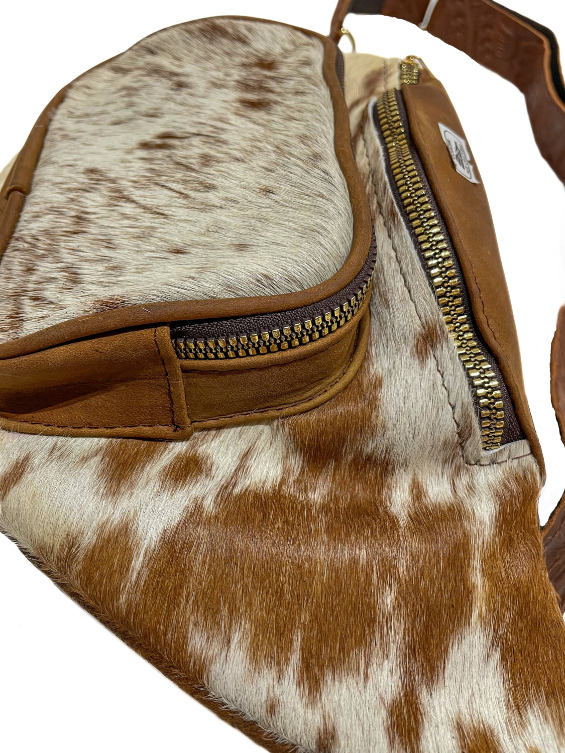 Close-up of light brown cow hair fanny pack showing front zippered pocket with natural cowhide and brown leather trim. 