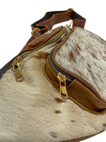 Close-up of light brown cow hair leather fanny pack showing detailed leather trim, stitching, and gold-tone zipper hardware. 
