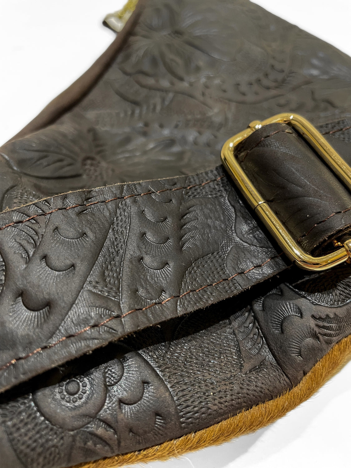 Close-up of brown cow hair leather fanny pack showing detailed leather engraving, stitching, and gold-tone zipper hardware. 