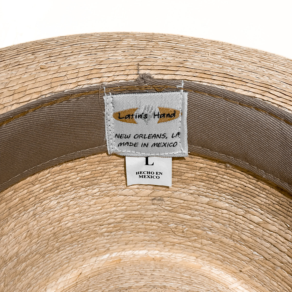 Close-up of the inside of a woven straw hat showing a sewn-in label that reads 'Latin's Hand' and 'New Orleans, LA Made in Mexico' alongside a size label marked 'L'. 