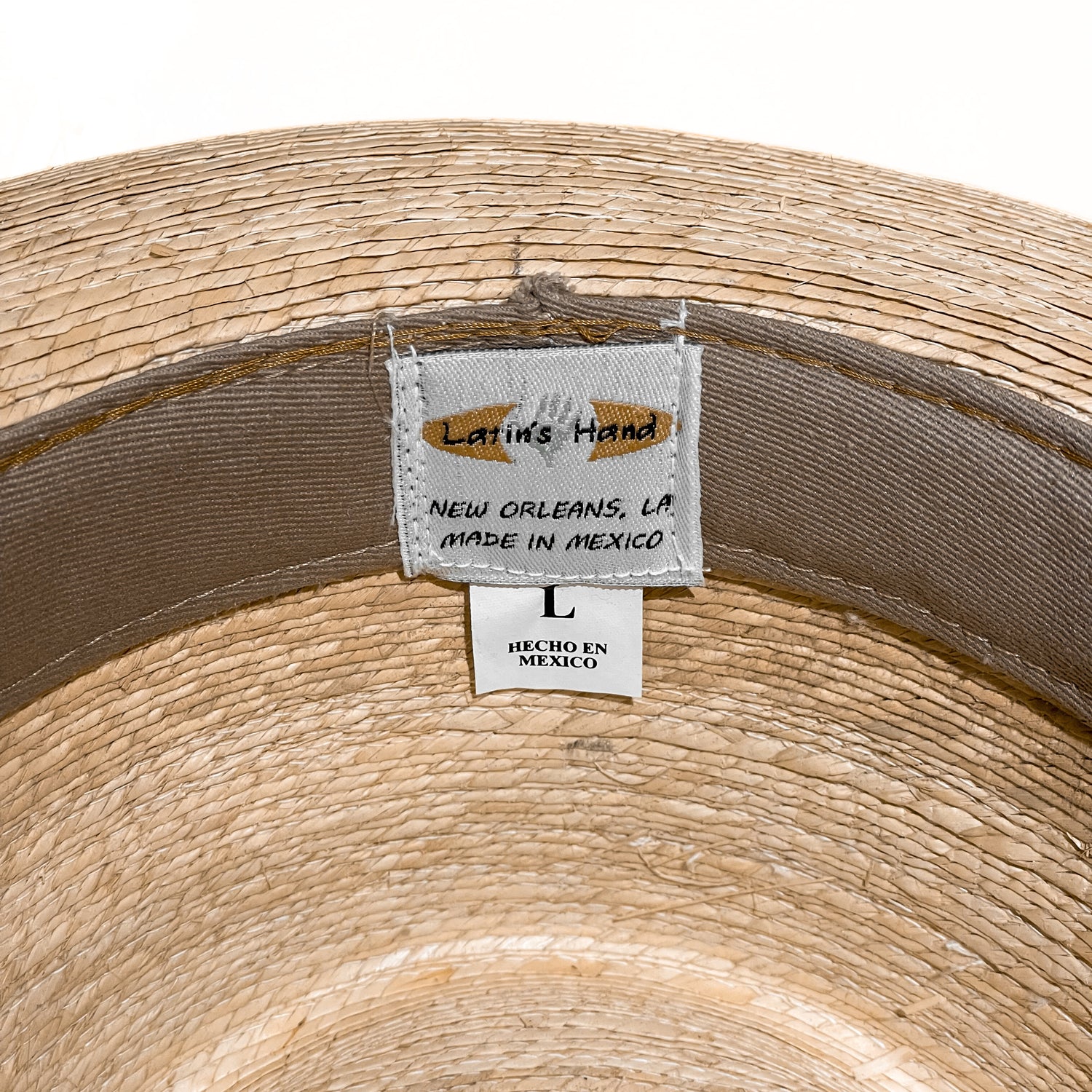 Close-up of the inside of a woven straw hat showing a sewn-in label that reads 'Latin's Hand' and 'New Orleans, LA Made in Mexico' alongside a size label marked 'L'. 